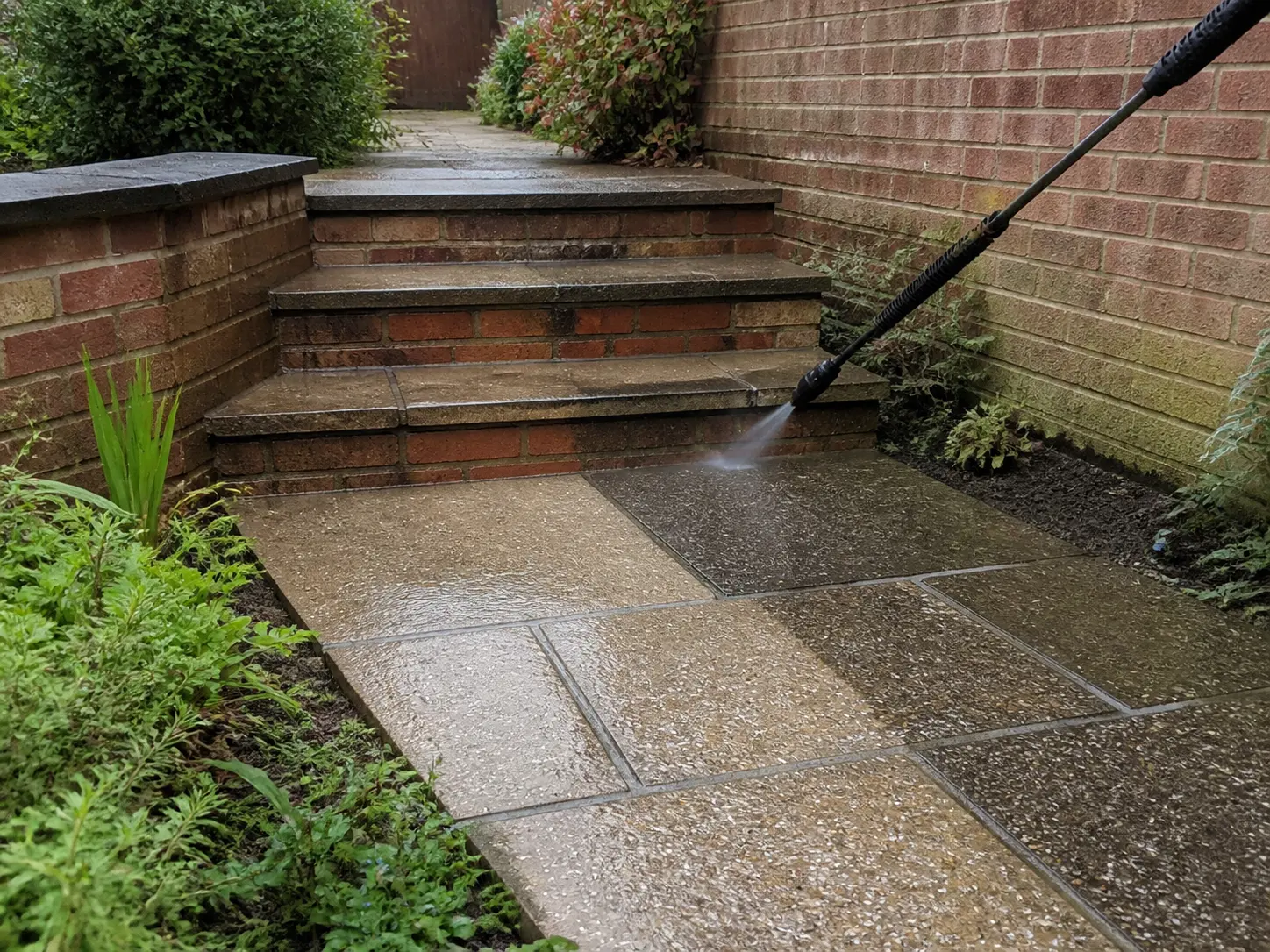 A paved garden path and masonry steps being cleaned with a pressure-washer lance.