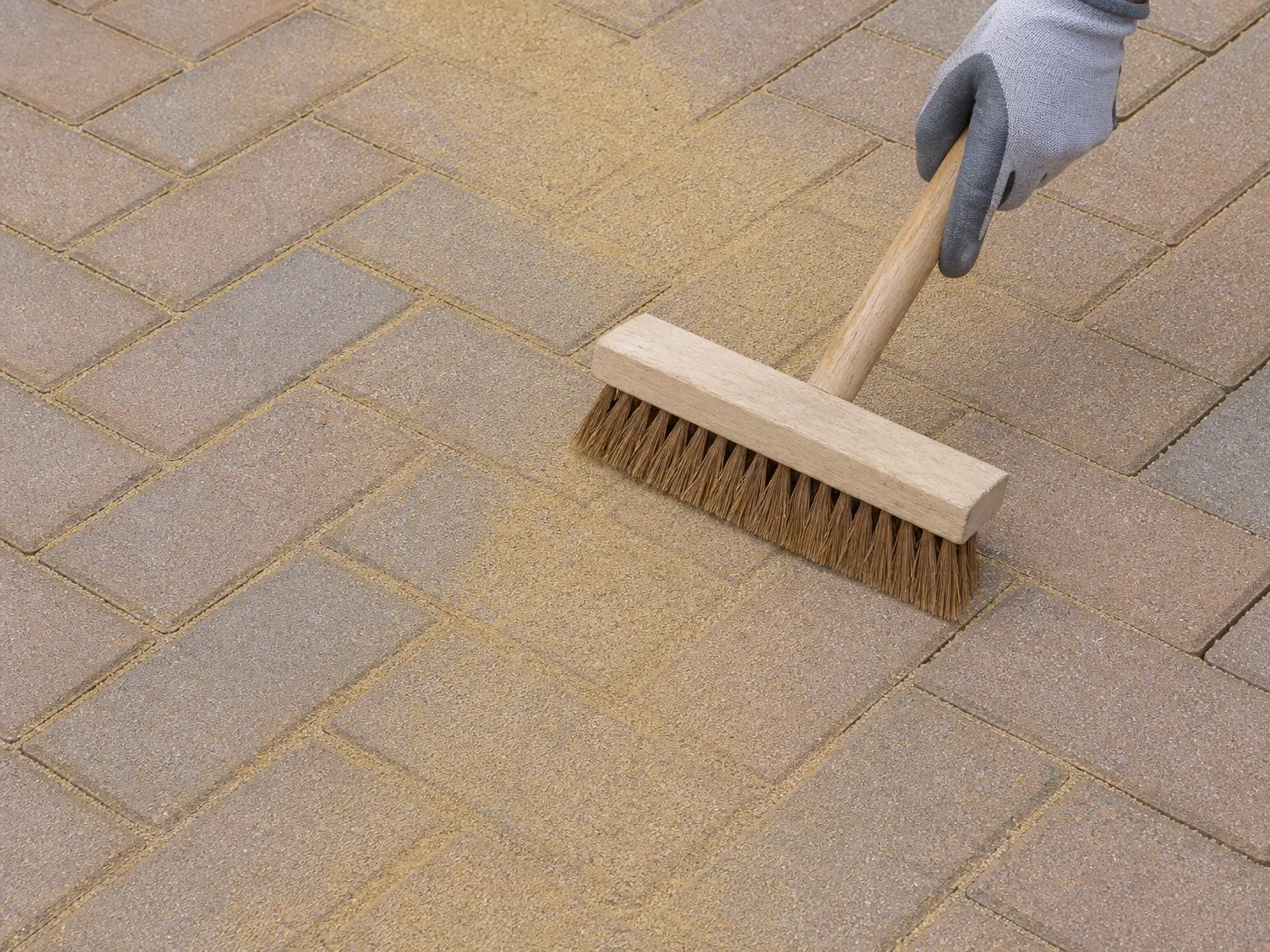 Dry jointing sand being brushed into the joints of clean block paving with a stiff broom.