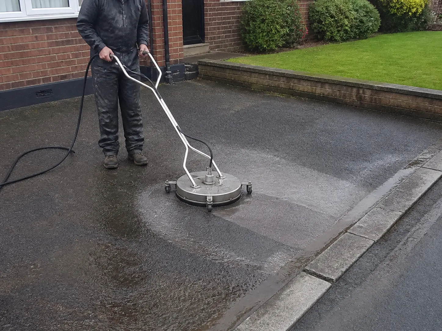 A rotary surface cleaner working across a damp, aged tarmac entrance.